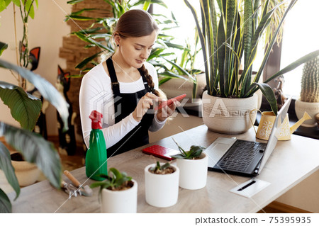 A florist girl uses her phone to take orders online at a flower shop. A florist girl uses her phone to take orders online at a flower shop. 75395935
