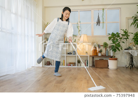 Cleaning: A young woman who wears a flooring wiper with a smile while dancing Cleaning: A young woman who wears a flooring wiper with a smile while dancing 75397948