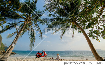 Scooter road trip. Woman alone on red motorbike in white clothes on sand beach by ocean. One girl caucasian tourist walk near tropical palm tree. Scooter road trip. Woman alone on red motorbike in white clothes on sand beach by ocean. One girl caucasian tourist walk near tropical palm tree. 75399606