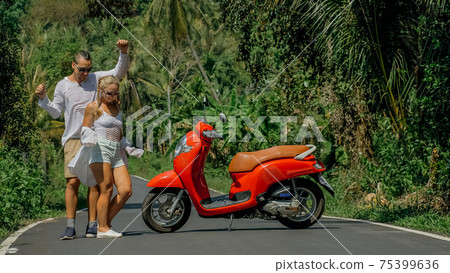 Love couple on red motorbike in white clothes, sunglasses on forest road trail trip. Dancing road. Two caucasian tourist woman man dance near scooter. 75399636