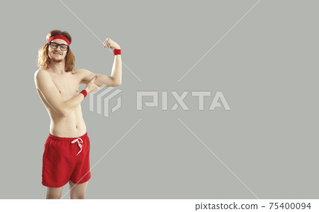 Funny thin young guy in red shorts with naked torso standing and showing small biceps 75400094