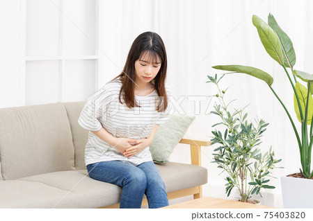 A young woman sitting on the sofa in the room and putting her hand on her belly 75403820