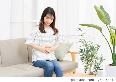 A young woman sitting on the sofa in the room and putting her hand on her belly 75403821