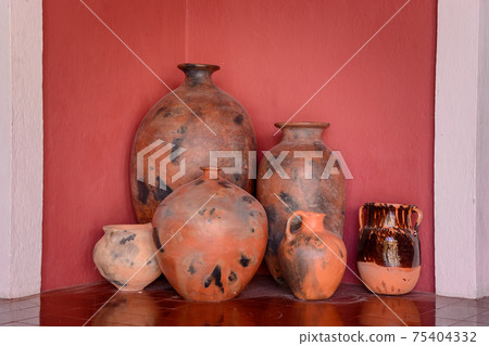 Several clay jugs with a narrow neck against a red wall. Several clay jugs with a narrow neck against a red wall. 75404332