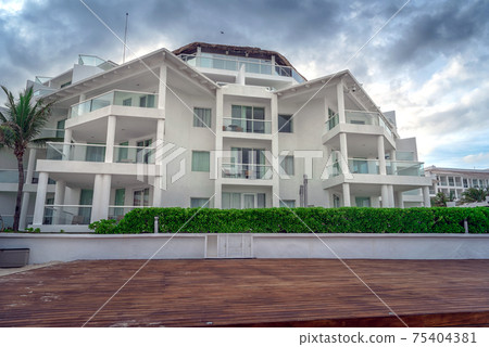 Large white building with a wooden terrace against a dark sky. Large white building with a wooden terrace against a dark sky. 75404381