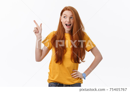 Portrait of happy young woman standing isolated over white wall background. Looking camera showing copyspace pointing 75405767
