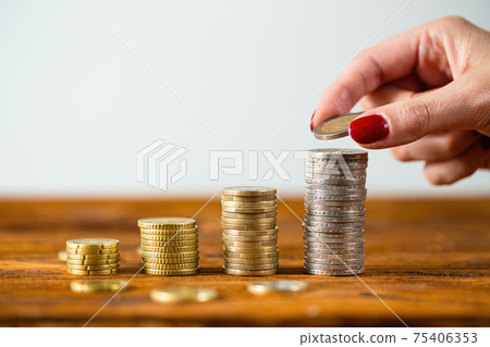 Female hand putting two euros onto stack on wooden table. Female hand putting two euros onto stack on wooden table. 75406353