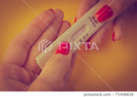 test for coronavirus on an orange background. medical analysis. a girl with a bright red manicure holds a coronavirus antibody test on her fingers 75406656