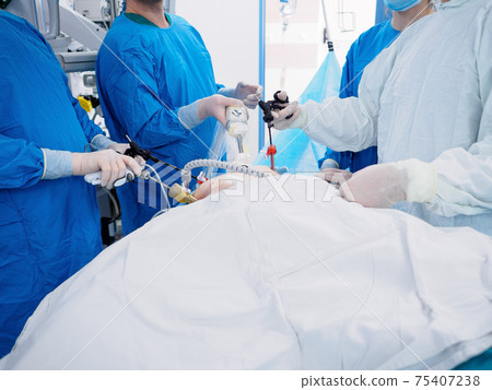 Surgeons in blue uniforms perform laparoscopic surgery using special medical equipment. Surgeons in blue uniforms perform laparoscopic surgery using special medical equipment. 75407238