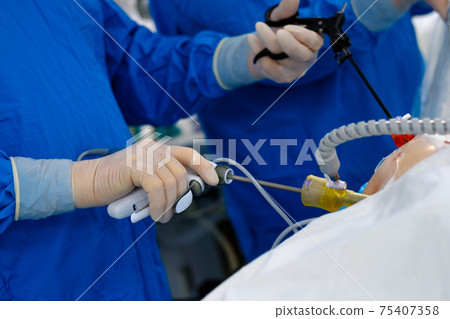 Surgeons in blue uniforms perform laparoscopic surgery using special medical equipment. Surgeons in blue uniforms perform laparoscopic surgery using special medical equipment. 75407358