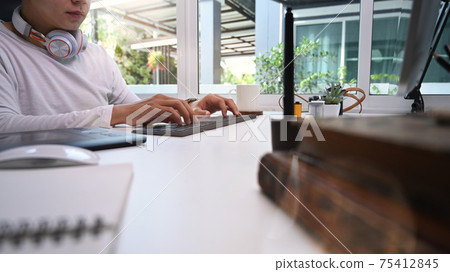 Graphic designer with headphone typing on keyboard at his creative workspace. Graphic designer with headphone typing on keyboard at his creative workspace. 75412845