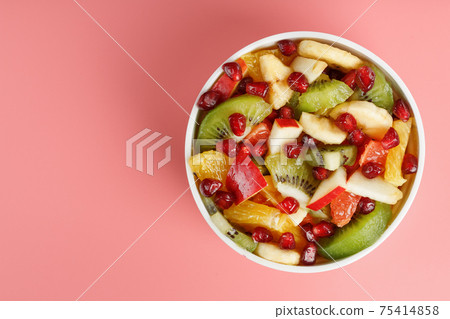 Salad of different juicy ripe fruits in a white cup on a pink background. 75414858