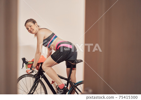 Woman trains at home on a stationary bike during a pandemic. Woman trains at home on a stationary bike during a pandemic. 75415300