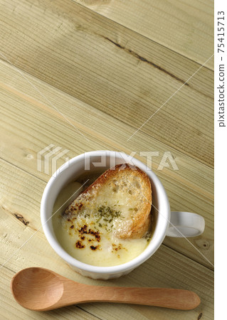 A bird's-eye view of onion soup and a wooden spoon containing browned French bread on cheese A bird's-eye view of onion soup and a wooden spoon containing browned French bread on cheese 75415713