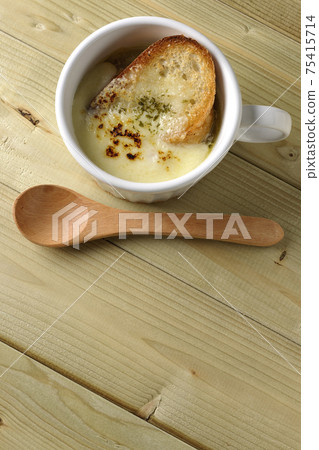 A bird's-eye view of onion soup and a wooden spoon containing browned French bread on cheese A bird's-eye view of onion soup and a wooden spoon containing browned French bread on cheese 75415714