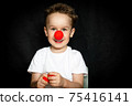 Boy with a clown red nose and red noses in hands. Red Nose Day. 75416141