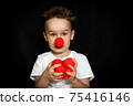 Boy with a clown red nose and red noses in hands. Red Nose Day. 75416146