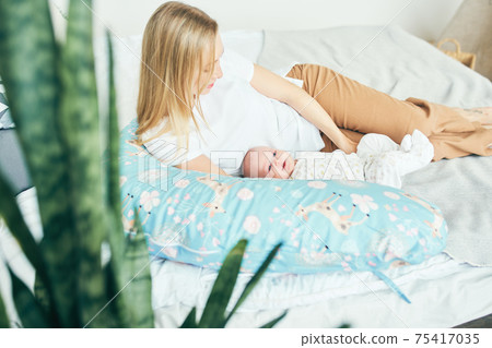 Young mother with baby in bed with a pillow for pregnant women. Young mother with baby in bed with a pillow for pregnant women. 75417035