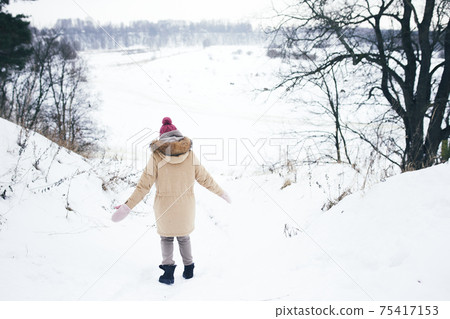 Beautiful woman walking among snowy trees in winter forest and coming down to river enjoying first snow. 75417153