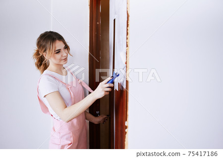 A girl in a pink work suit repaints an old door. Renovation and new life for old things. A girl in a pink work suit repaints an old door. Renovation and new life for old things. 75417186