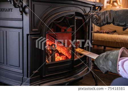 A photo of putting firewood in a wood stove (fireplace) 75418381