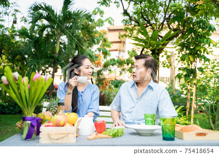 Senior couple with food and drink picnic in garden park talking care together 75418654