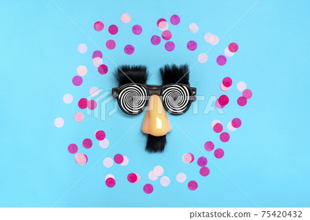funny face - fake eyeglasses, nose and mustache, confetti, sequins on blue background Happy fools day concept 1st April party Holiday card funny face - fake eyeglasses, nose and mustache, confetti, sequins on blue background Happy fools day concept 1st April party Holiday card 75420432