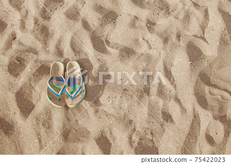BEACH PARAPHERNALIA ON THE SAND: SANDALS. TRAVEL TO THE SEA 75422023
