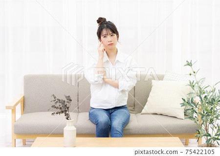 一個年輕女子坐在窗邊的沙發上和思考 一個年輕女子坐在窗邊的沙發上和思考 75422105