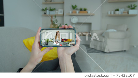 A female student hands takes an extra lesson distance. Video chat between student and teacher. Smartphone screen view. A female student hands takes an extra lesson distance. Video chat between student and teacher. Smartphone screen view. 75422107