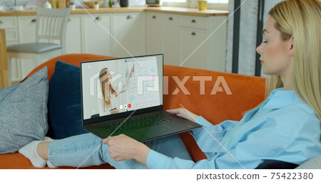 A female student takes an extra lesson distance. Video chat between student and teacher. Over shoulder laptop blur screen view. 75422380