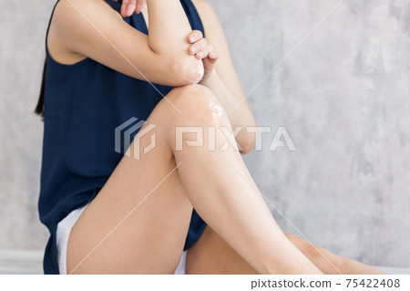 Woman applying cream to elbows and knees 75422408