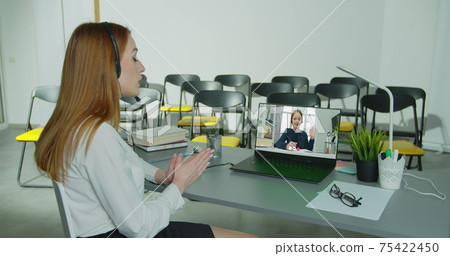 Little kid girl talk by videocall app, laptop screen view over woman shoulder sit at desk. Distance learning course due corona virus. Tutoring on-line using modern tech. 75422450