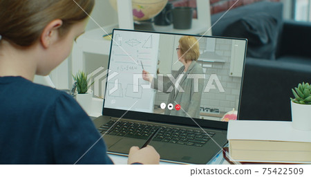 Schoolgirl is studying at home with a tutor making notes in a notebook. Distance learning online video chat with a teacher. 75422509