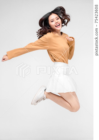 happiness, freedom, motion and people concept - smiling young woman jumping in air over gray background 75423608