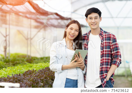 Smart young asian farmer  using tablet to check quality and quantity of organic hydroponic vegetable garden at greenhouse 75423612
