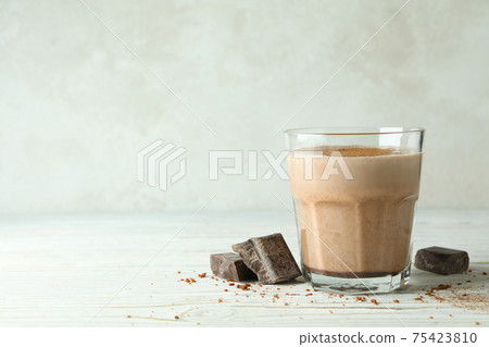 Glass of chocolate milkshake and chocolate pieces on wooden table 75423810