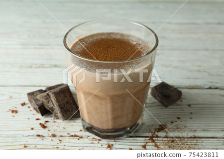 Glass of chocolate milkshake and chocolate pieces on wooden table 75423811
