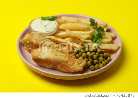 Plate with fried fish and chips, pea and sauce on yellow background Plate with fried fish and chips, pea and sauce on yellow background 75423875