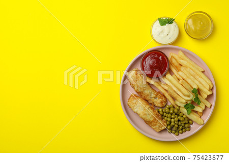 Plate with fried fish and chips, pea and sauces on yellow background Plate with fried fish and chips, pea and sauces on yellow background 75423877