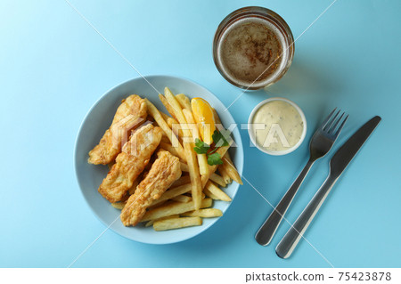 Concept of tasty eating with fried fish and chips, and beer on blue background Concept of tasty eating with fried fish and chips, and beer on blue background 75423878