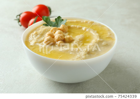 Bowl of hummus and tomatoes on white textured background Bowl of hummus and tomatoes on white textured background 75424339