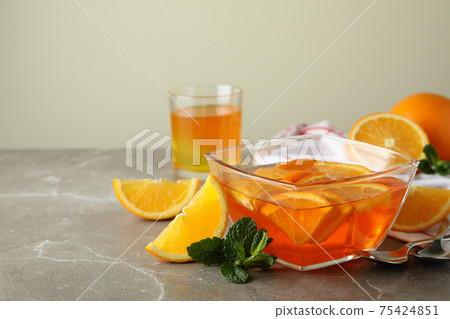 Concept of dessert with bowl of orange jelly with orange slices on gray table Concept of dessert with bowl of orange jelly with orange slices on gray table 75424851