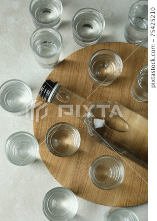 Board with bottle and shots of vodka on white textured background 75425210
