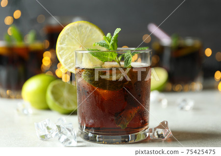Glass of Cuba Libre on white textured table against blurred lights Glass of Cuba Libre on white textured table against blurred lights 75425475