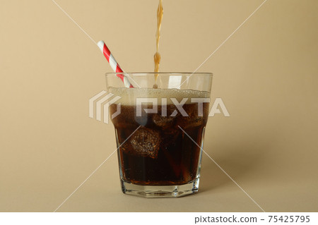 Cola is poured into a glass on beige background Cola is poured into a glass on beige background 75425795