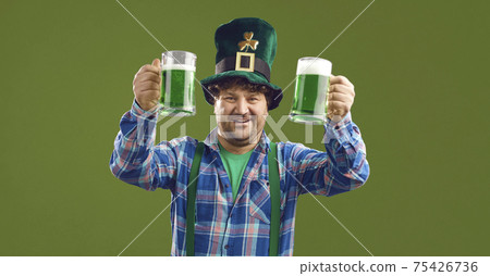 Irish man in Patrick hat with two raised beers isolated on green copy space Irish man in Patrick hat with two raised beers isolated on green copy space 75426736