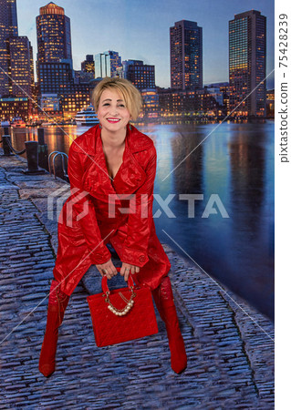 woman in red raincoat boots and a bag posing on the embankment of the night city 75428239