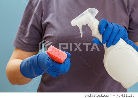 Woman holding a bottle of washing liquid and a sponge on a blue background. 75431135