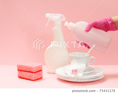 Woman's hand in protective glove with bottle of dishwashing liquid on a pink background. Woman's hand in protective glove with bottle of dishwashing liquid on a pink background. 75431178